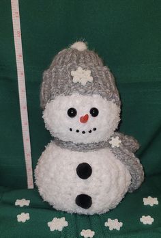 a stuffed snowman sitting on top of a green blanket next to a measuring tape