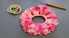 a crocheted pink flower sits next to some scissors and yarn on a table