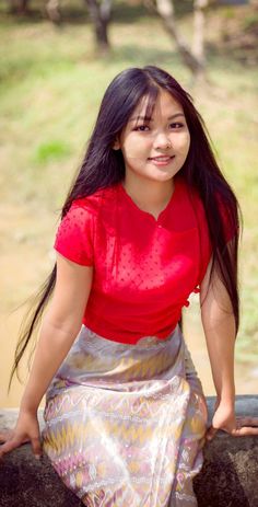 a young woman sitting on top of a stone wall next to a tree and grass covered field