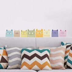 a group of cats sitting on top of pillows in front of a white couch with colorful chevroned pillows