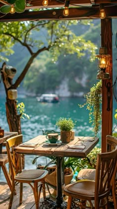 an outdoor dining area with wooden tables and chairs near the water, surrounded by greenery