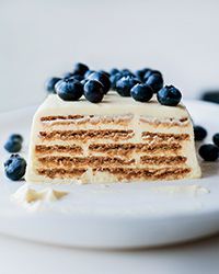 a white plate topped with a slice of cake covered in frosting and blueberries