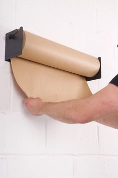 a man holding a roll of brown paper on top of a white brick wall next to a black piece of cardboard