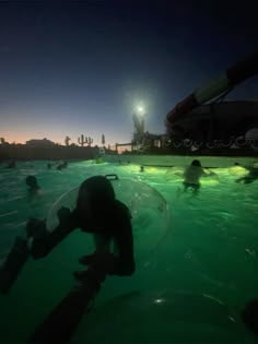 people swimming in the water at night with lights on and one person holding onto an object