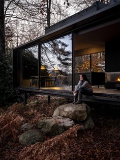 a woman sitting on the edge of a wooden deck next to a house in the woods