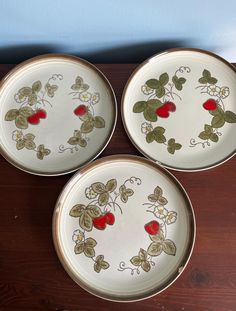 three white plates with red and green designs on them sitting on a wooden table next to a blue wall