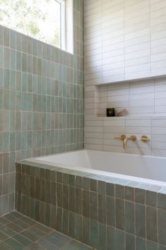 a bath tub sitting under a window next to a tiled wall and floor in a bathroom