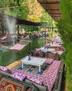 an outdoor seating area with hammocks, tables and chairs on the water's edge