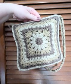 a crocheted granny bag is being held up by a woman's hand