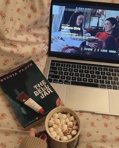 a laptop computer sitting on top of a bed next to a cup of marshmallows