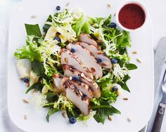 a white plate topped with lettuce and blueberries next to a cup of sauce