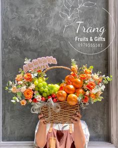 a woman holding a basket full of fruit in front of a chalkboard wall with the words trang fruits and gifts written on it