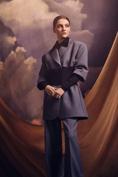 a woman standing in front of a painting wearing a gray suit and black shirt with her hands on her hips