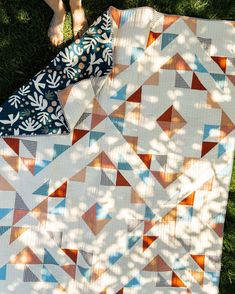 a person laying on the grass with their feet up next to a quilted blanket