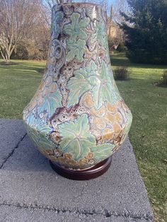 a large vase sitting on top of a cement slab next to a grass covered field