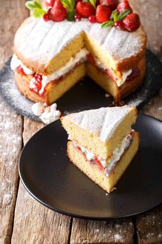 a cake with strawberries on top is cut in half and sits on a black plate