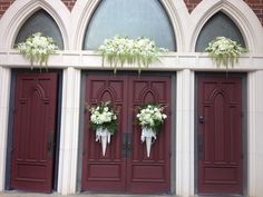 two red doors with white flowers and greenery on the side of them, in front of a church