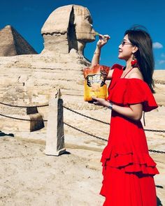 a woman in a red dress is holding a book and standing near the sphinxs