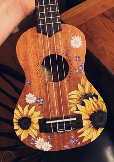 a wooden ukulele with sunflowers painted on it's body and strings