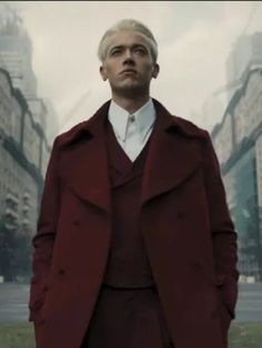 a man in a red coat is standing in the middle of a city with tall buildings