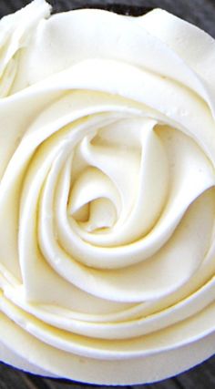 a white rose shaped cake sitting on top of a wooden table covered in frosting