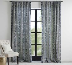 a white chair sitting in front of a window with curtains on the windowsills