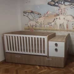 a baby's room with a crib, dresser and wall mural