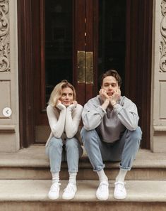 two people sitting on the steps in front of a door with their hands under their chins