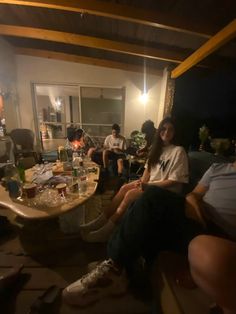 a group of people sitting around a table in a living room at night with lights on