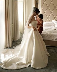 two women in wedding gowns are looking at the bride's dress on her bed