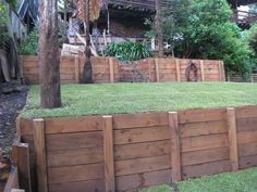 a wooden fence with grass growing on top and trees in the backgrouds