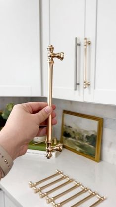 a person is holding a golden door handle on a white kitchen counter with gold hardware