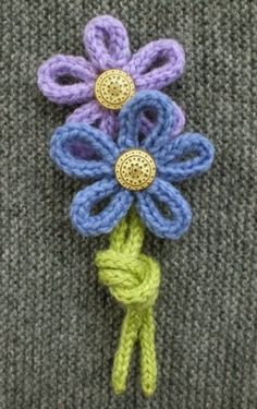 a crocheted flower on top of a gray sweater with green and blue yarn