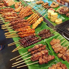 many skewers of food are being displayed on banana leaf trays at an outdoor market