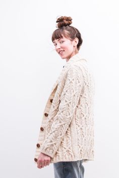 a woman wearing a sweater and jeans standing in front of a white wall with her hair in a bun