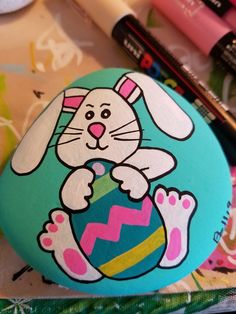 a painted rock with an image of a bunny holding an easter egg and crayons next to it