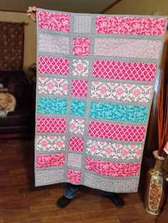 a person holding up a quilt in front of a couch