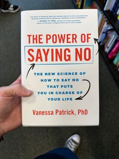 the power of saying no book being held up by someone's hand in front of bookshelves