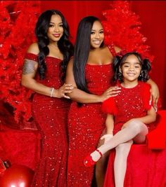 three women in red dresses standing next to each other near a christmas tree and presents