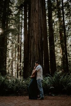 a man and woman standing in front of a large tree with their arms around each other