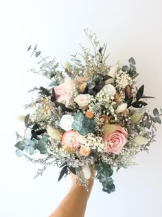 a hand holding a bouquet of flowers against a white background with greenery and leaves