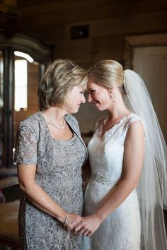 two women standing next to each other in front of a mirror wearing wedding gowns