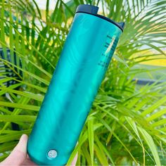 a person holding up a green cup in front of some palm trees and plants on the ground