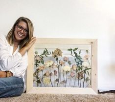 a woman sitting on the floor next to an art piece with flowers painted on it