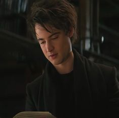 a young man sitting at a table reading a book with his eyes closed while looking down