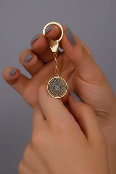 a woman holding onto a gold keychain that has a medallion on the front