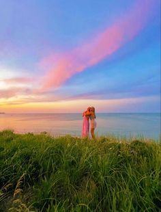 a woman standing on top of a lush green hillside next to the ocean at sunset