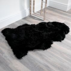 a black sheepskin rug is on the floor in front of a table and mirror