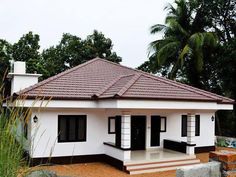 a small white house with black shutters and a red tiled roof in front of some trees