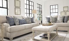 a living room filled with furniture and pillows on top of a white floor next to windows